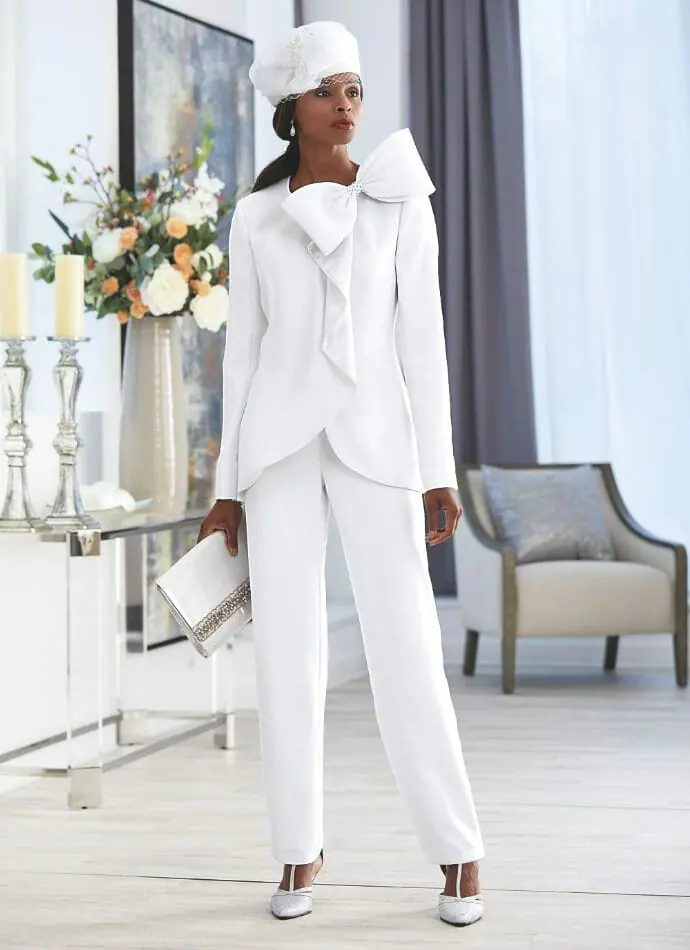 Black woman in white pantsuit with bow on jacket front and white hat