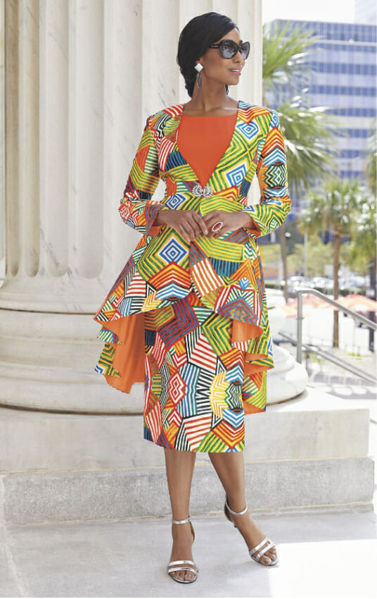 A black woman in a multi-print orange wardrober including the hi-low jacket, skirt, orange tank and orange pant.