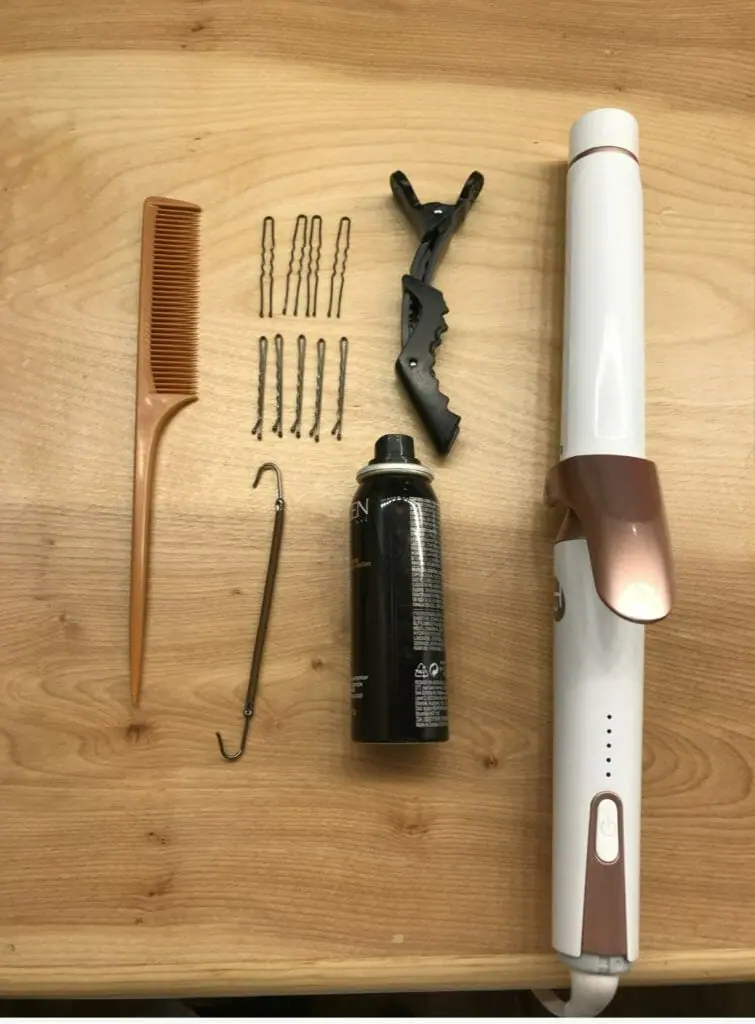 A small gold comb, bobby pins, hair tie, hairspray, and a white curling iron.