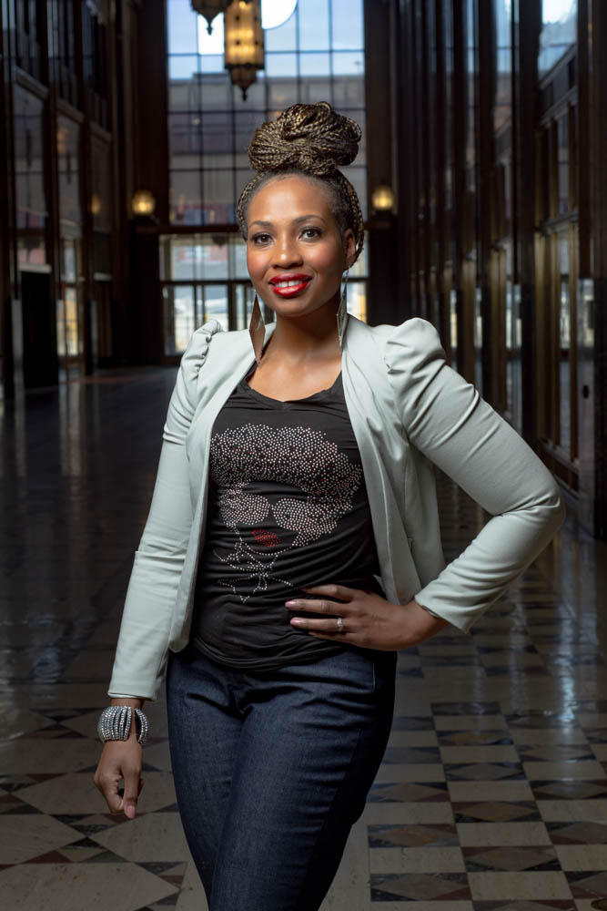An African-American woman in a black top with a bling lady head applique, jeans and a white jacket.