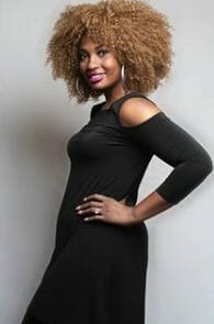 An African-American woman with big Afro hair in a black dress with a shoulder cut out.