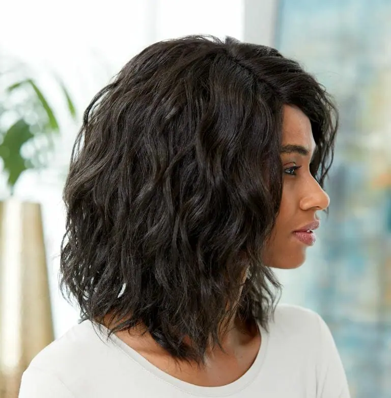 A profile of an African-American woman in a white top and long, wavy, side-parted off-black Vivica Fox wig.