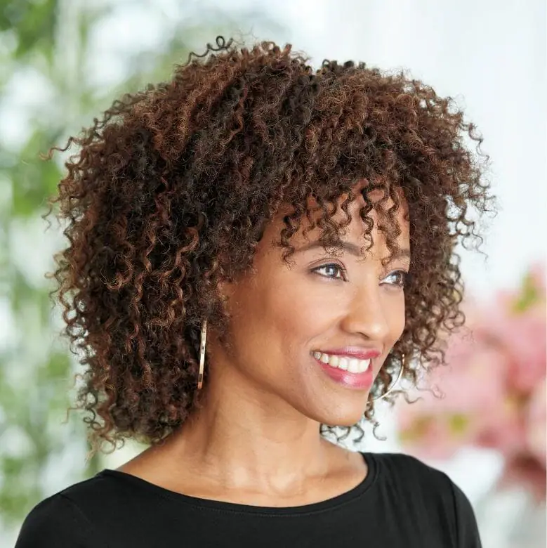A smiling African-American woman wearing a black top, drop earrings, and a brown Afro-style wig by Vivica Fox.