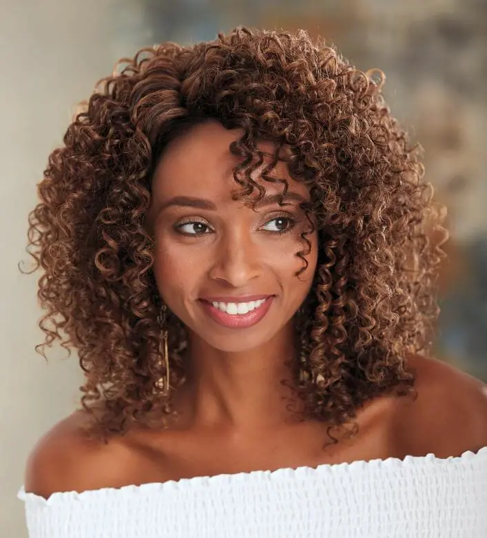 A smiling African-American woman wearing an off-shoulder top and a full, auburn Afro-style wig by Vivica Fox.