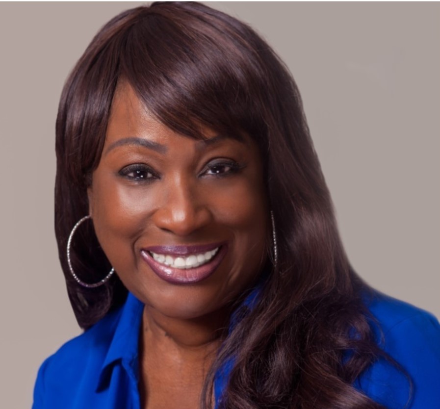 Ashro Woman of the Week, Alicia, a smiling black woman with smooth burgundy hair and bangs, in a blue dress.