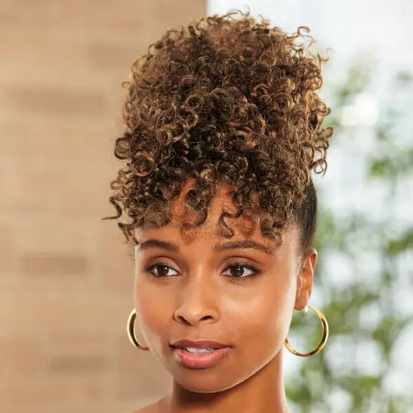 An African-American woman wearing a short, auburn wavy Vivica Fox wig with bangs, and gold hoop earrings.