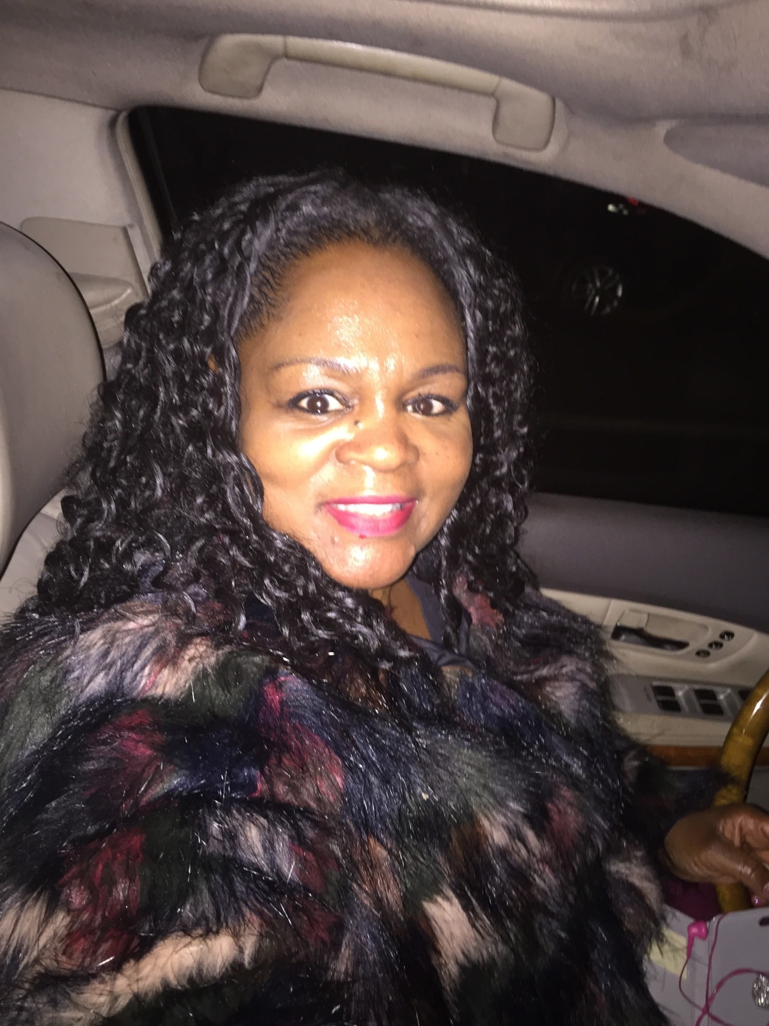 Ashro Woman of the Week, Latasha, a black woman with long curly hair, in her car, wearing a black print top.