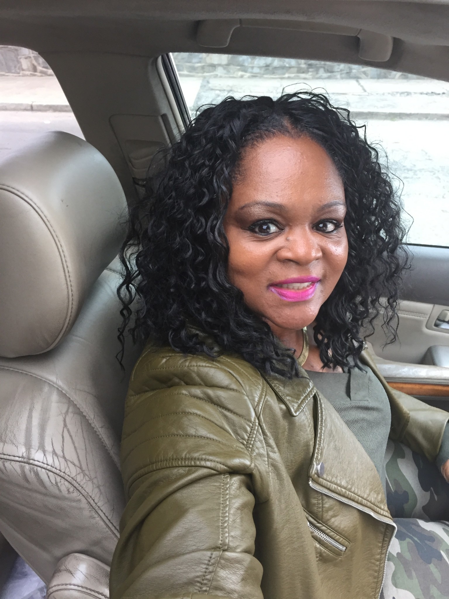 Ashro Woman of the Week, Latasha, a black woman with long curly hair, in her car, wearing a green leather jacket.