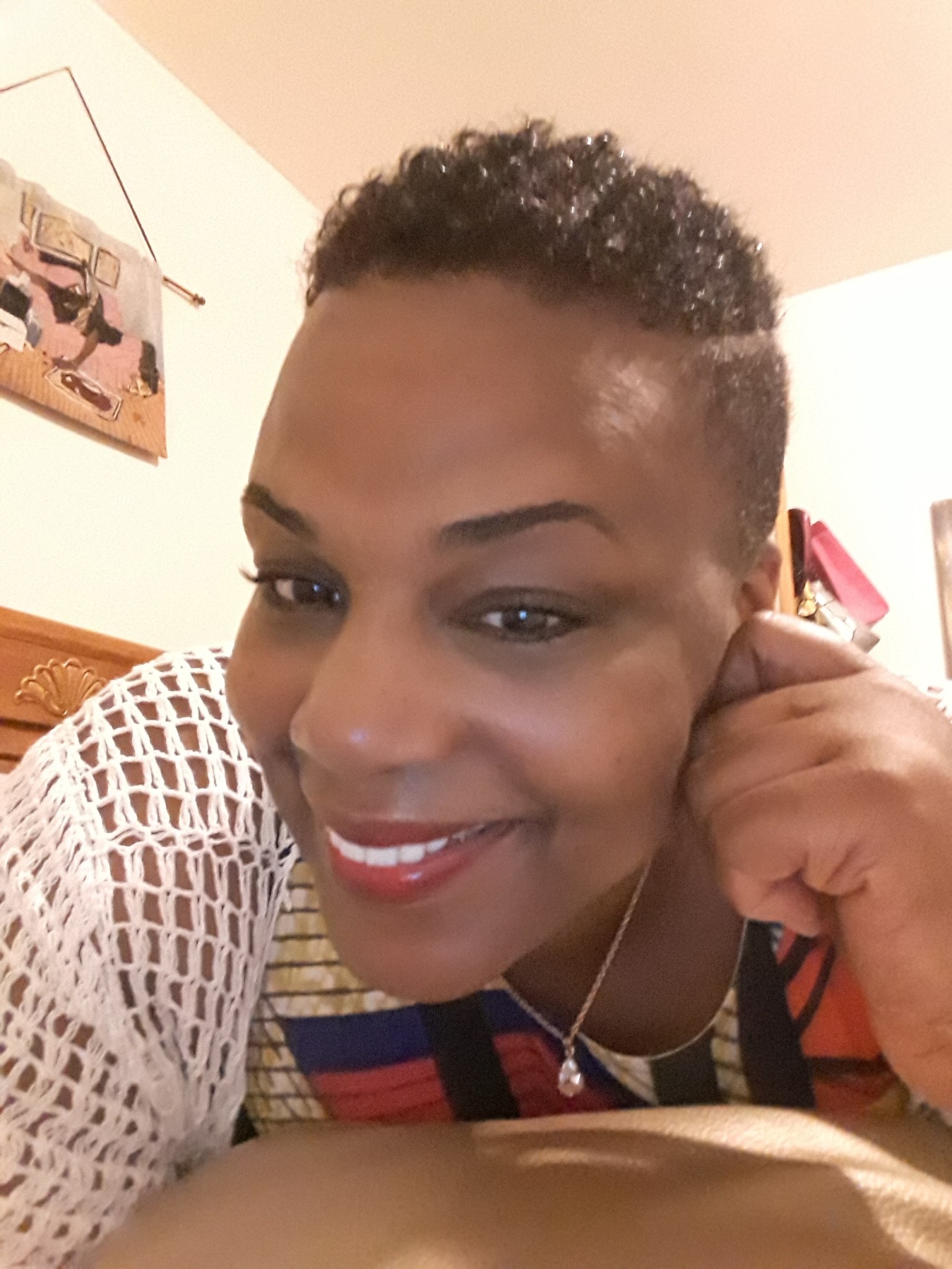 Close-up of MICHELLE, a smiling black woman with short hair, wearing a white dress, with her hand to her cheek.