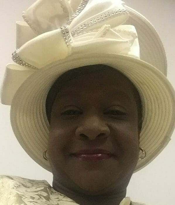 DYNITA H. from Texas, a smiling African-American woman in a pale yellow jacket dress with a matching hat.