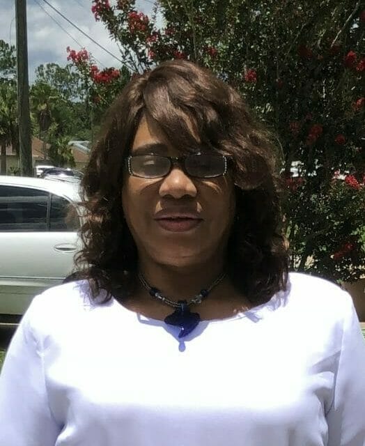 FRANCES LARRY, an African-American woman in a white dress with a peplum and flared sleeves.