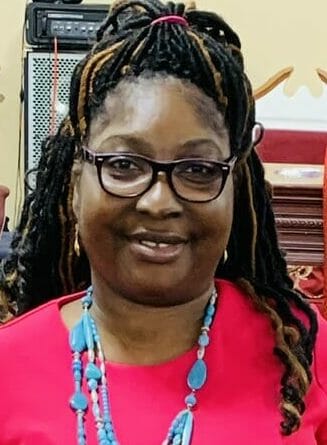 SHON, a smiling African-American woman in a hot pink dress with teal necklace, bag and shoes.