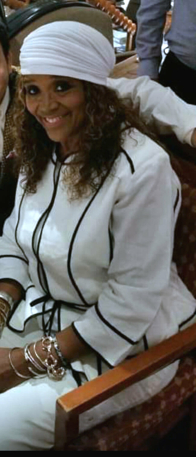 Ashro Woman of the Week CAROLYN, a smiling African-American woman in a white suit and matching headwrap.