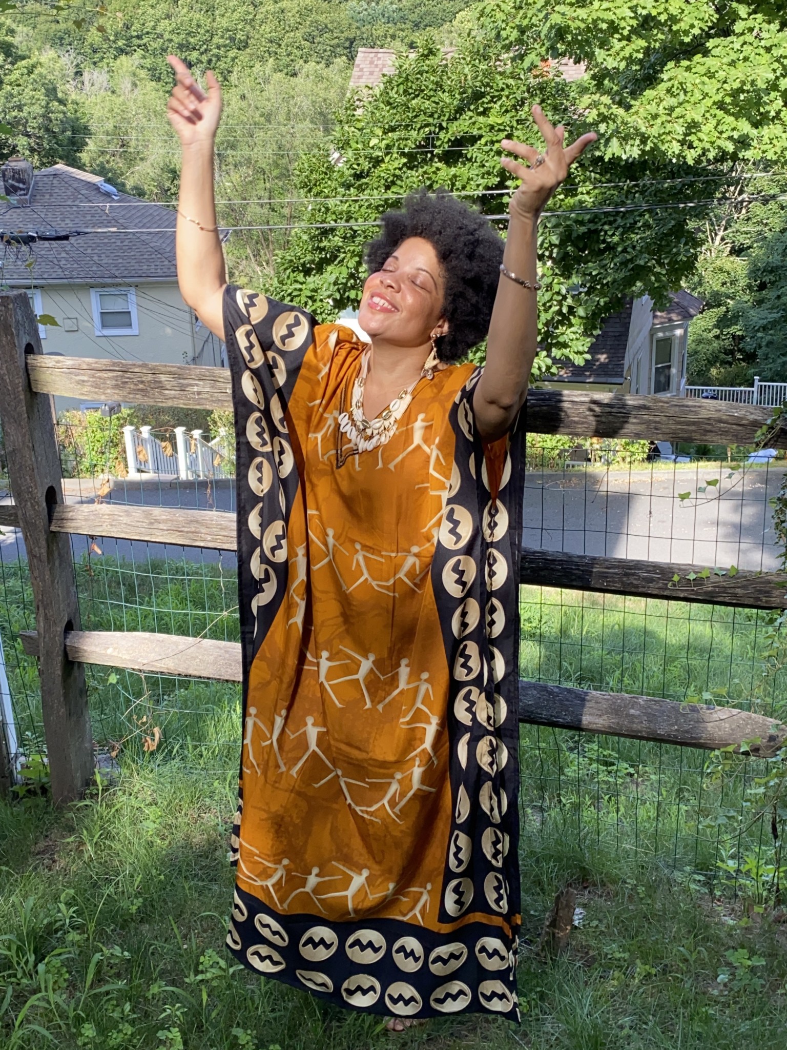 A black woman wearing an orange and Afrocentric patterned caftan.