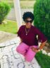 black woman wearing maroon top and pink pants sitting