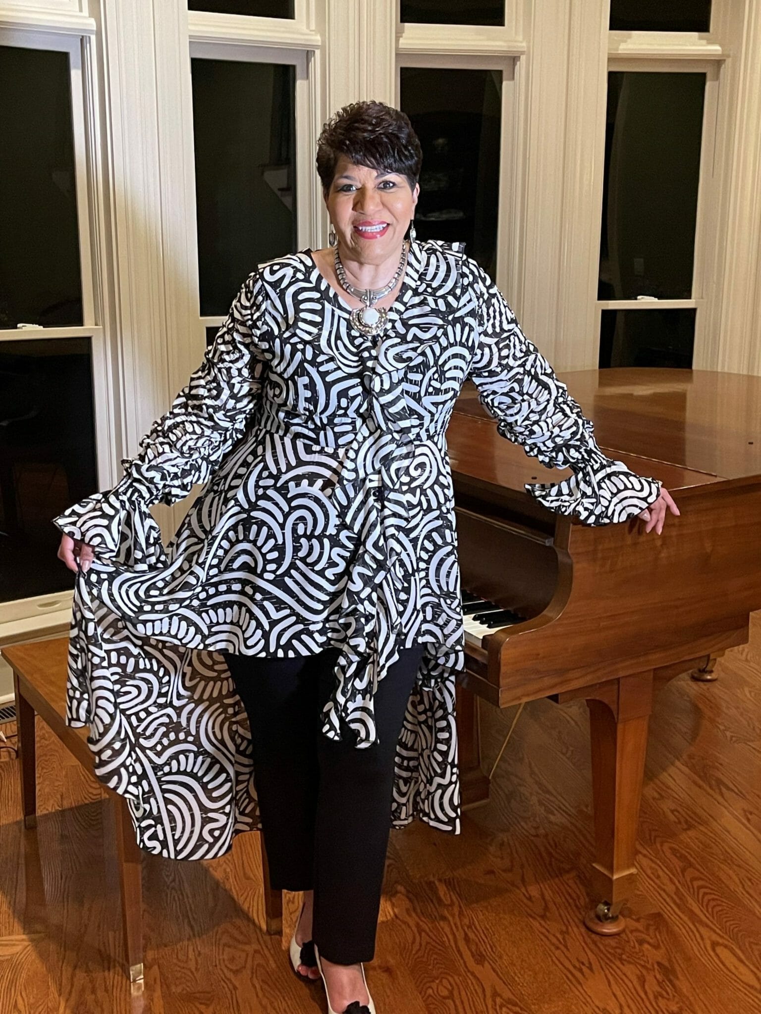Ashro customer wearing a black and white flowy top, posing next to a piano