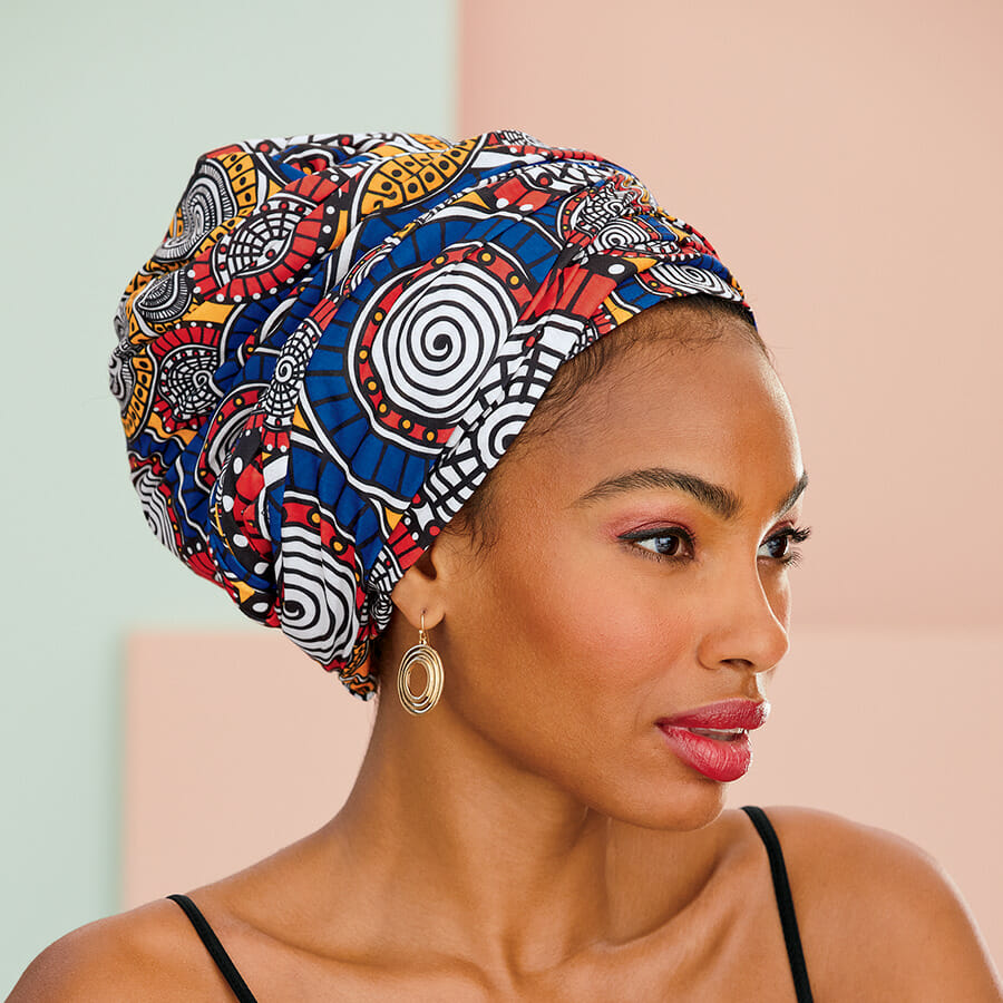 African American woman with red, blue, yellow, black and white print headwrap and circular gold earrings with black top.