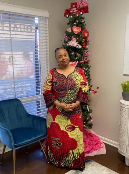 Woman standing in front of a tall thin Christmas tree in a red and yellow dress