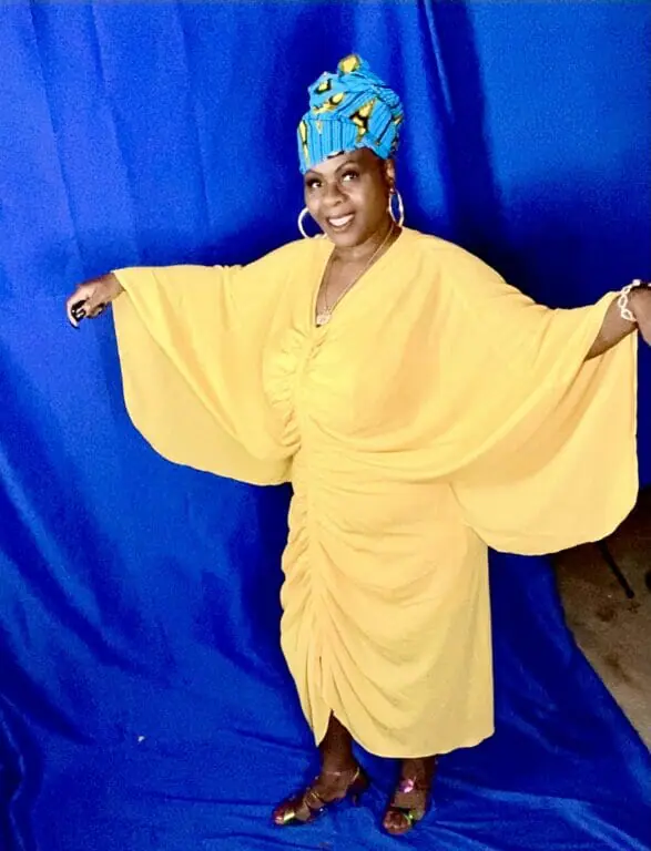 Black woman wearing yellow dress and blue headwrap.