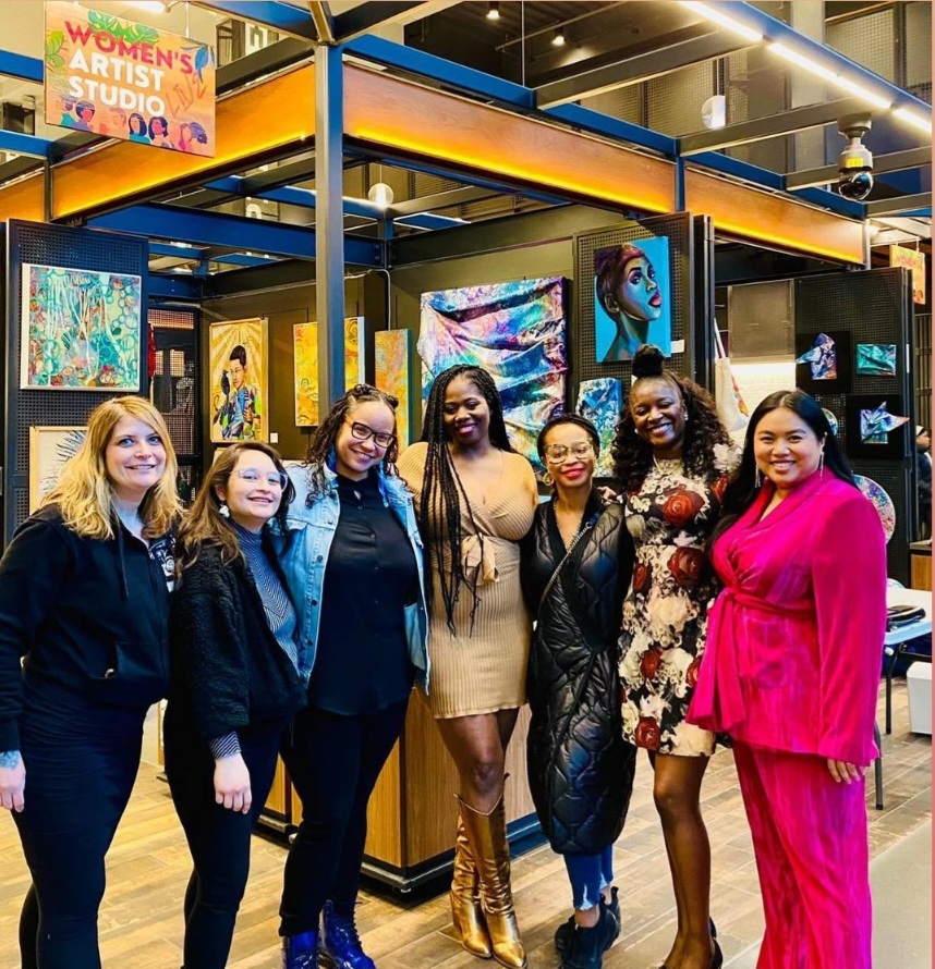 A group of women standing in front of art display posing for picture