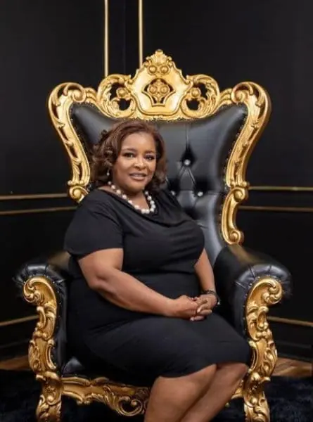 woman in a black dress sitting in a black chair with gold trim
