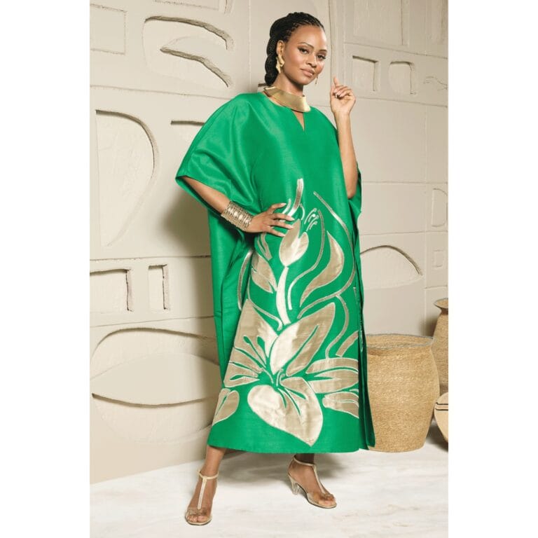 Woman in green kaftan with gold floral print, gold jewelry, and heels.