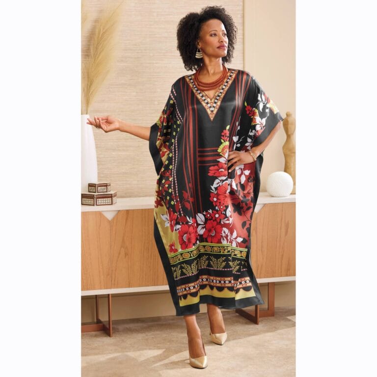 A woman in a vibrant floral kaftan poses confidently in a stylish, modern interior with wooden furniture and decor.