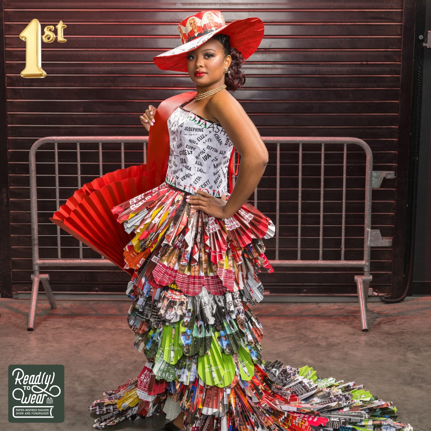 A woman in a vibrant, layered dress made of magazine pages poses confidently, wearing a matching hat and holding a fan.