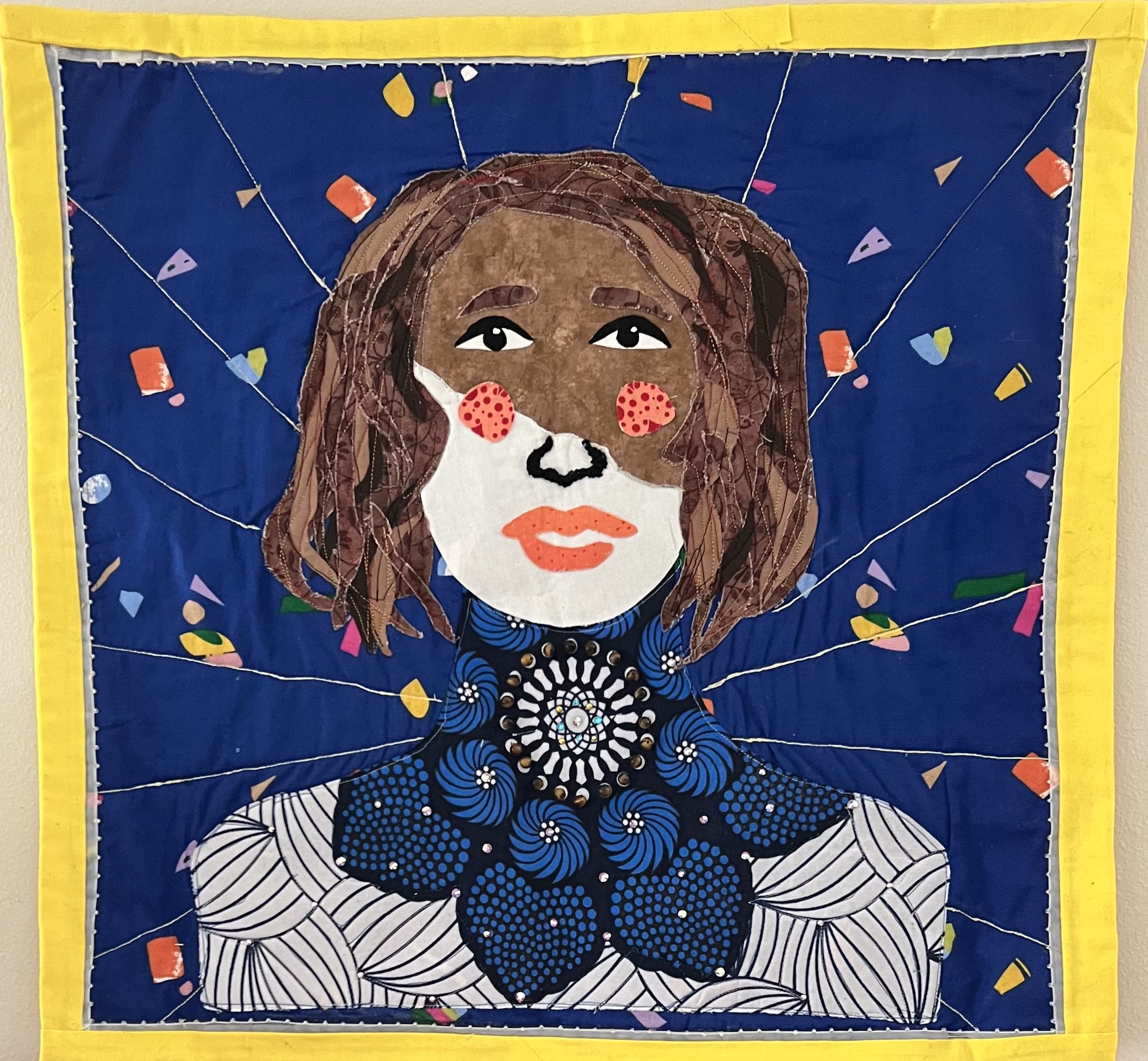 Colorful textile art featuring a woman with curly hair, bold facial features, and a decorative patterned collar.