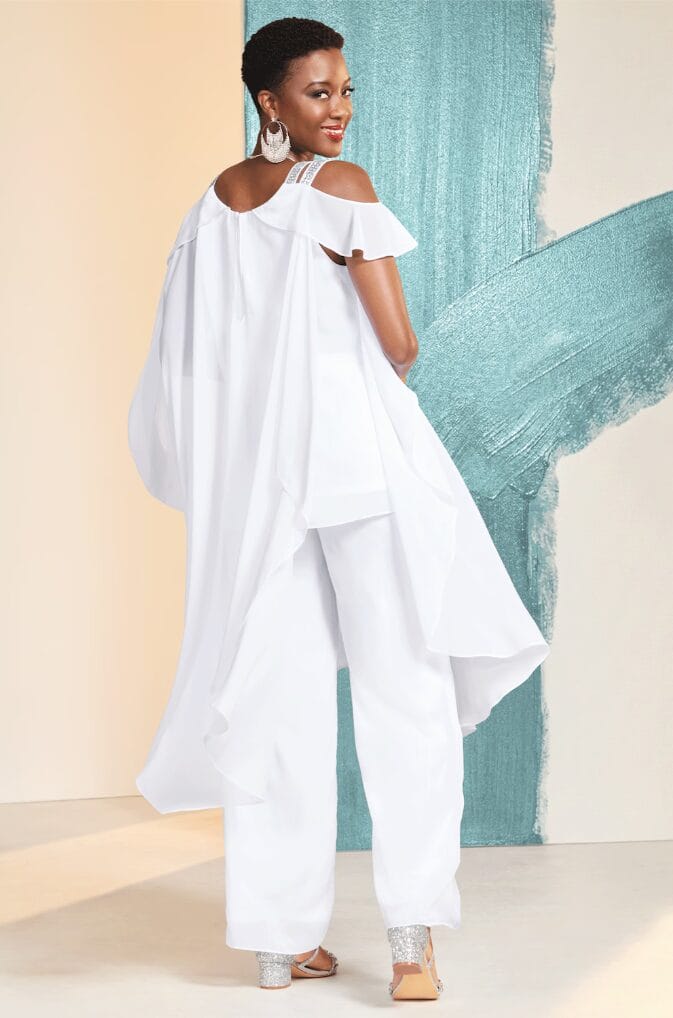 A woman in a flowing white outfit with ruffled sleeves and sparkling heels poses against a colorful backdrop.