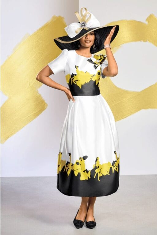 black model wearing silk white dress with black and yellow print and large fancy hat.