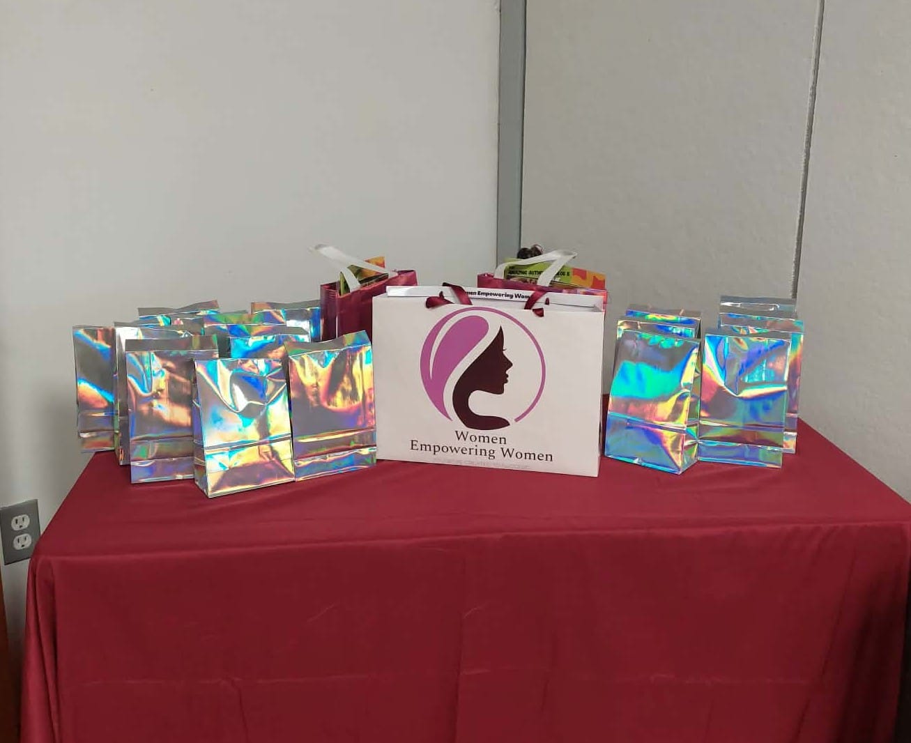 Holographic gift bags arranged on a red table, featuring a prominent "Women Empowering Women" logo.
