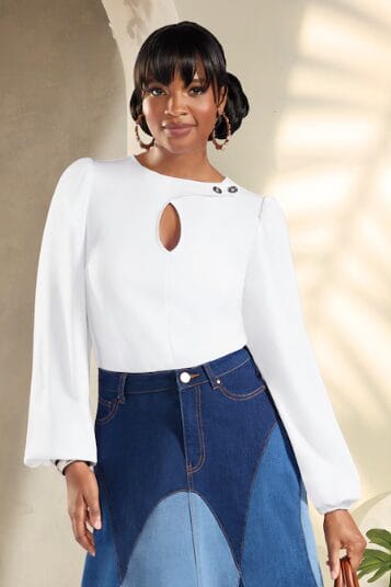 Black woman wearing a ponte top with a crossover keyhole neckline and accent buttons on one side, with a hidden working button on the other. The top features full, gathered sleeves with added volume created by elasticized edging.