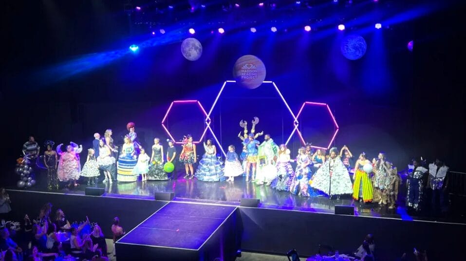 The image showcases all contestants on the stage in their outfits showcasing creative unity.