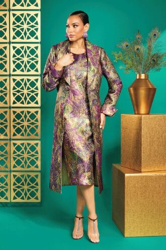 Woman in a shimmering purple and gold brocade dress and matching coat, posing with peacock feathers.