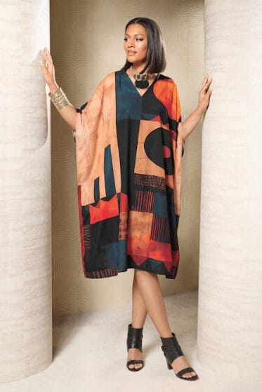 Woman in a colorful abstract print kaftan dress and black heeled sandals.