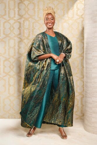 Woman in a gold turban and a flowing green and gold brocade robe over teal pants.