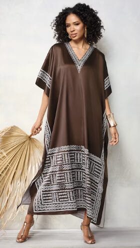 Woman in a flowing brown kaftan with white geometric trim and a large dried palm frond.