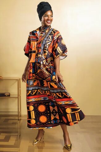 Woman in a black headwrap and a colorful, patterned maxi dress with gold heels.