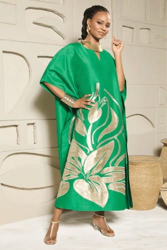 Woman in green kaftan with gold floral print, gold jewelry, and strappy heels.