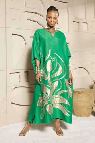 Woman in a green kaftan with gold floral print, gold jewelry, and clear heels.