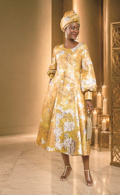 Woman in a gold patterned dress and headwrap, holding a small purse.