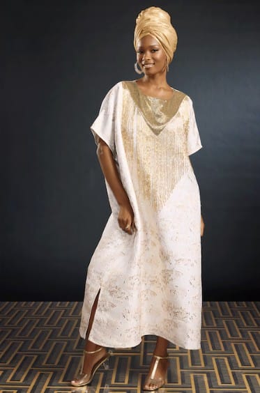 Woman in a gold-turban and a white and gold patterned kaftan dress.