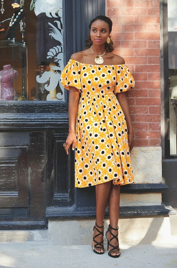 African-American woman in yellow, black, white sunburst print off the shoulder dress from Reuben Reuel Collection