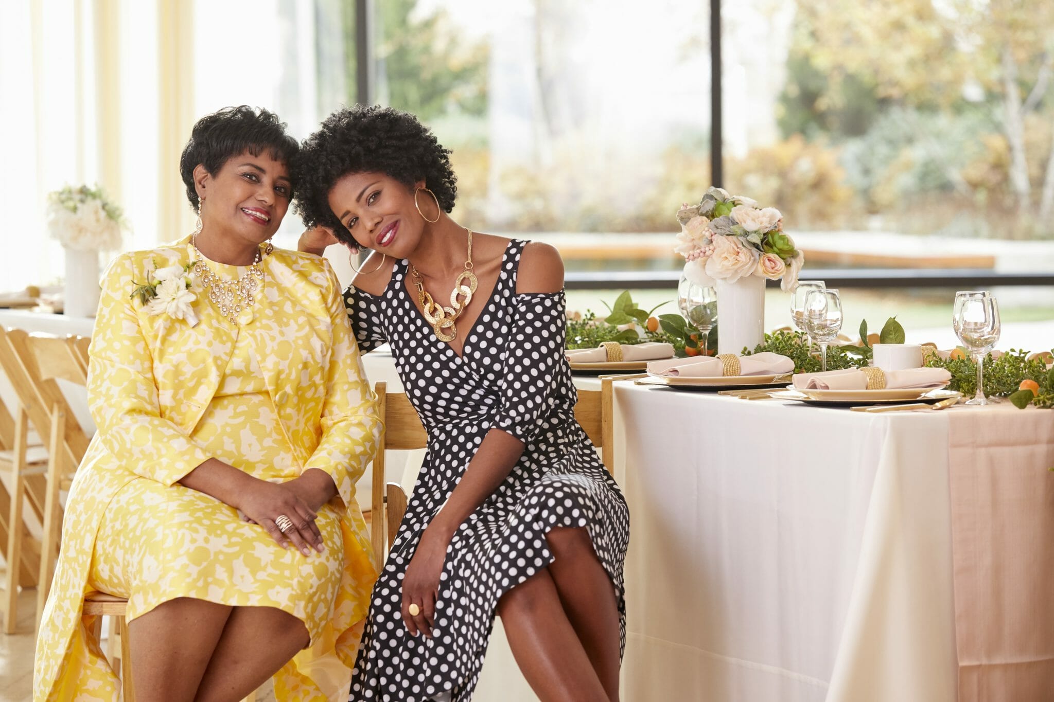 African-American mother and daughter smiling, sitting at table with heads tilted