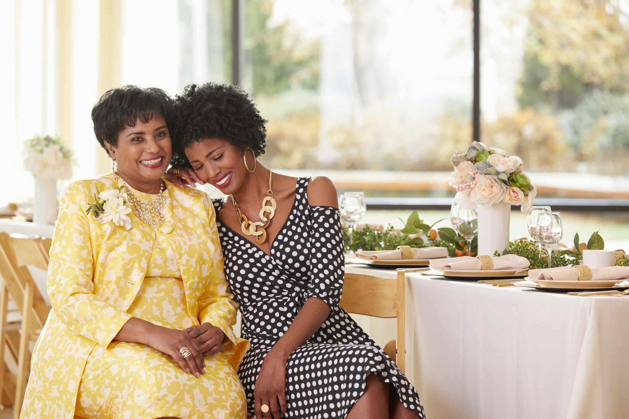African-American mother and daughter smiling, sitting at table with heads tilted