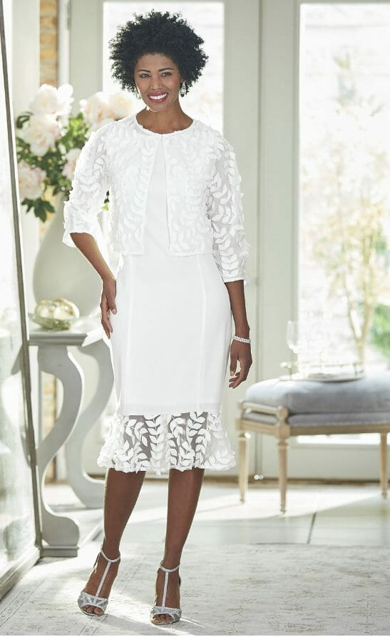 A black woman wearing a white mesh jacket dress embellished with fabric leaves.
