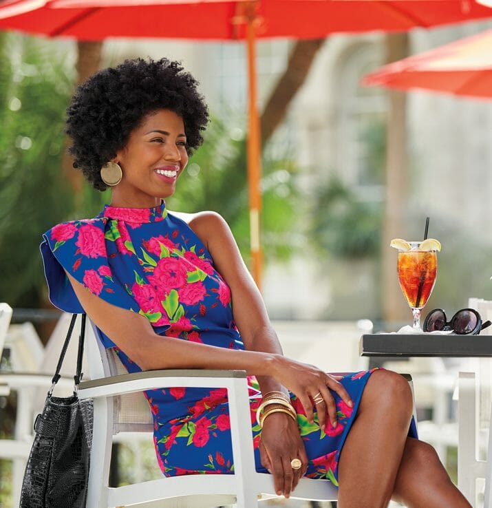 black woman in blue and pink flower print dress sitting at outside cafe