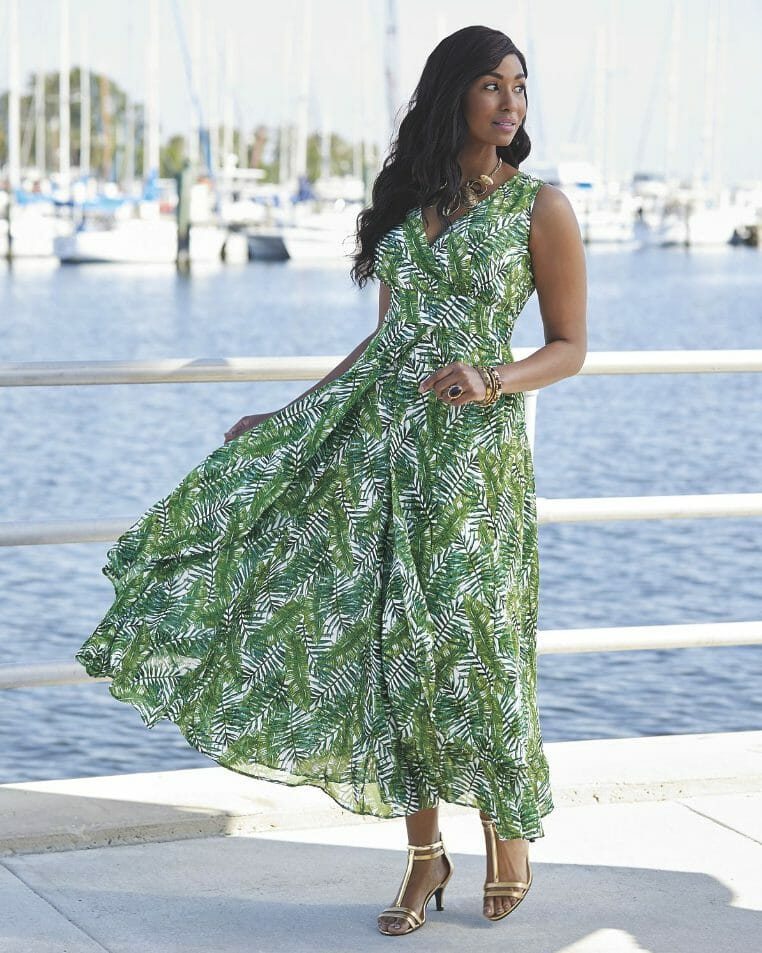 A black woman with long hair, wearing a sleeveless green and white palm-leaf print dress with a full skirt.