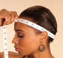 A black woman with a tape measure at the natural hairline of her head, measuring around her head.